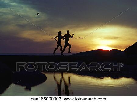 Stock Photo - Couple running near water at sunset, silhouette. Fotosearch