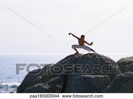 Picture - Man doing tai chi on a rock near the sea.. Fotosearch