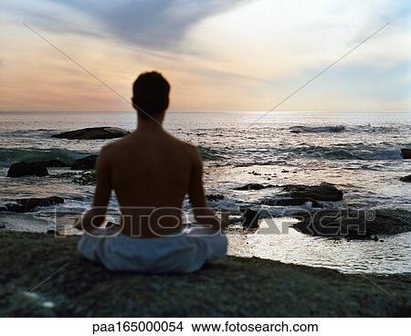 Man sitting in lotus position in front of sea, rear view, silhouette. View Large Photo Image Picture - Man sitting in lotus position in front of sea, rear view, silhouette.. Fotosearch