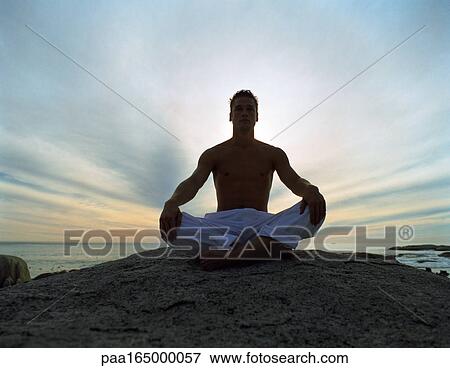 Man sitting indian style on rock, backlit, full length, sky and sea in background View Large Photo Image Stock Photo - Man sitting indian style on rock, backlit, full length, sky and sea in background. Fotosearch