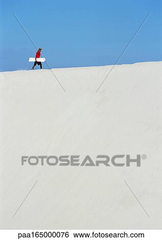 Man walking across dune with snowboard View Large Photo Image Stock Photograph - Man walking across dune with snowboard. Fotosearch