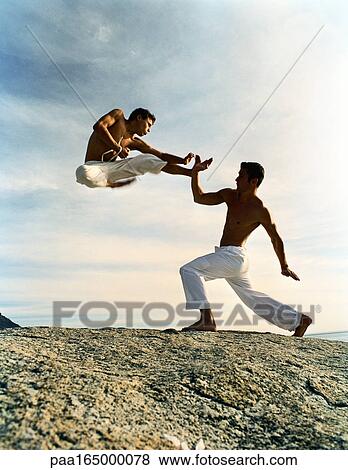 Two men performing martial arts on rocky ground, one in mid-air, full length View Large Photo Image Stock Photo - Two men performing martial arts on rocky ground, one in mid-air, full length. Fotosearch