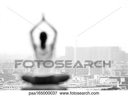 Stock Photo - Woman sitting in yoga position, overlooking city, rear view, blurred, focus on background, b&w. Fotosearch