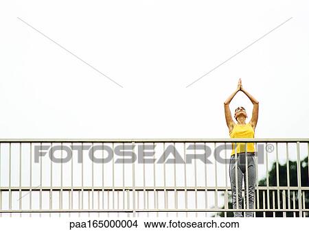 Woman standing on bridge, hands over head, low angle view. View Large Photo Image Picture - Woman standing on bridge, hands over head, low angle view.. Fotosearch