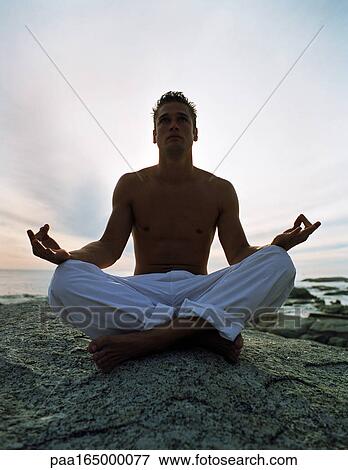 Young man sitting on rock in lotus position in front of sea View Large Photo Image Stock Photo - Young man sitting on rock in lotus position in front of sea. Fotosearch