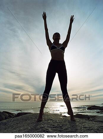 Young woman standing tiptoe, arms up, full length, on rocky shore, sky and seascape in background View Large Photo Image Stock Image - Young woman standing tiptoe, arms up, full length, on rocky shore, sky and seascape in background. Fotosearch