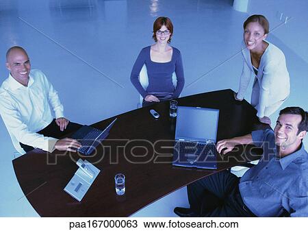 Stock Image - Business people around desk, smiling, elevated view. Fotosearch