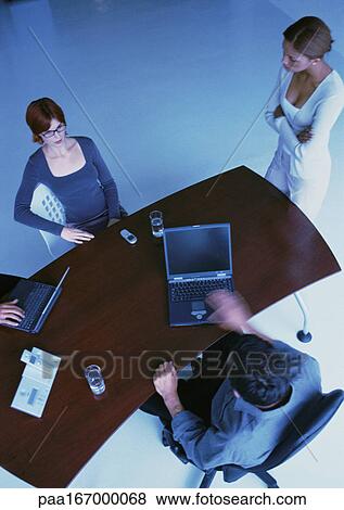 Business people around desk, two with laptops, elevated view View Large Photo Image Stock Photo - Business people around desk, two with laptops, elevated view. Fotosearch