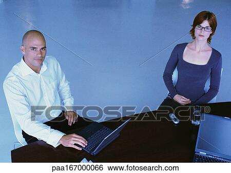 Businessman and woman sitting at desk View Large Photo Image Stock Photograph - Businessman and woman sitting at desk. Fotosearch