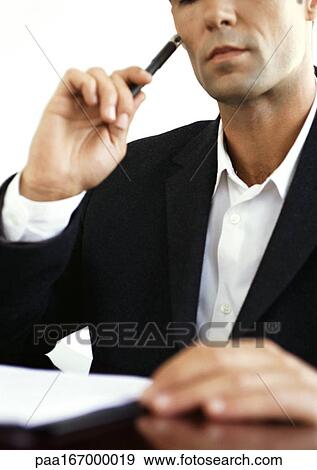 Businessman at desk, holding pencil, close-up View Large Photo Image Stock Photo - Businessman at desk, holding pencil, close-up. Fotosearch
