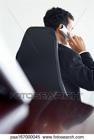 Businessman at desk using phone, rear view View Large Photo Image Stock Photography - Businessman at desk using phone, rear view. Fotosearch