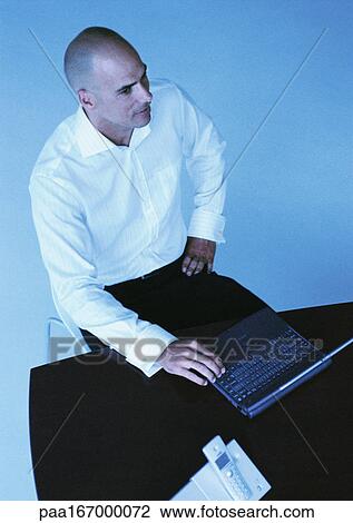Businessman sitting at desk with laptop computer, high angle view View Large Photo Image Stock Image - Businessman sitting at desk with laptop computer, high angle view. Fotosearch