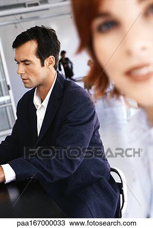 Businessman sitting at desk, woman smiling View Large Photo Image Stock Image - Businessman sitting at desk, woman smiling. Fotosearch