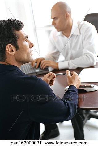 Businessmen sitting at desk View Large Photo Image Stock Image - Businessmen sitting at desk. Fotosearch