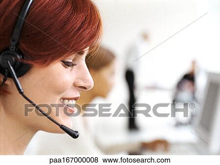 Stock Photo - Woman wearing headset in office, side view, close-up. Fotosearch