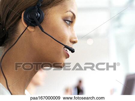 Stock Photo - Woman wearing headset in office, side view, close-up. Fotosearch