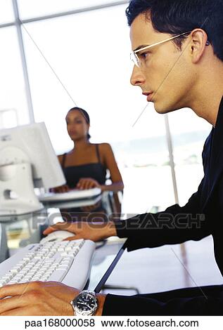 Businessman and businesswoman working at desks, side view of man in foreground View Large Photo Image Stock Photo - Businessman and businesswoman working at desks, side view of man in foreground. Fotosearch