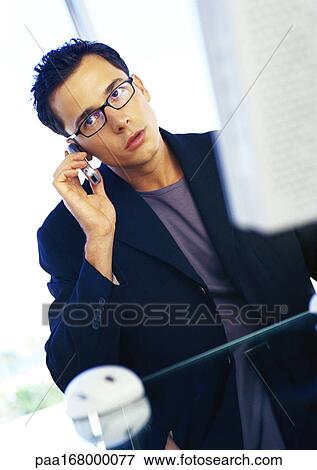 Businessman sitting at computer, using cell phone View Large Photo Image Stock Photo - Businessman sitting at computer, using cell phone. Fotosearch