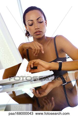 Businesswoman sitting at computer, looking at watch View Large Photo Image Stock Image - Businesswoman sitting at computer, looking at watch. Fotosearch