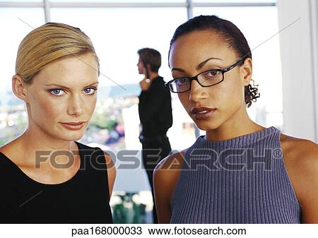 Businesswomen looking into camera, man in background View Large Photo Image Stock Image - Businesswomen looking into camera, man in background. Fotosearch