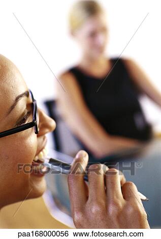 Two businesswoman, one holding pen near mouth, close-up View Large Photo Image Stock Photograph - Two businesswoman, one holding pen near mouth, close-up. Fotosearch