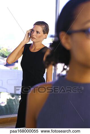 Two businesswomen, one holding cell phone View Large Photo Image Stock Photography - Two businesswomen, one holding cell phone. Fotosearch