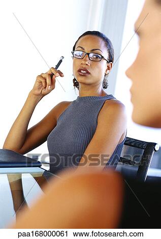 Stock Image - Two businesswomen, one holding up pen, portrait. Fotosearch