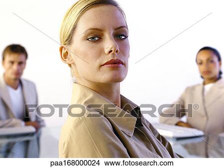 Woman looking into camera, colleagues in background, portrait View Large Photo Image Picture - Woman looking into camera, colleagues in background, portrait. Fotosearch