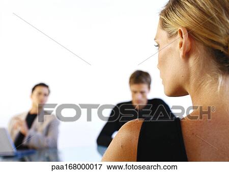 Stock Photo - Woman sitting across from two men in office, rear view. Fotosearch