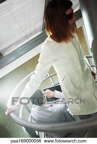 Stock Photograph - Man sitting on stairs, woman coming up stairs, high angle view. Fotosearch