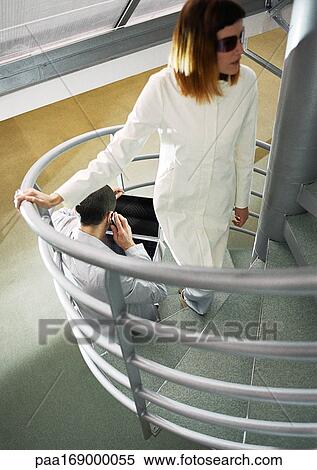Stock Photography - Man sitting on stairs, woman coming up stairs, high angle view. Fotosearch