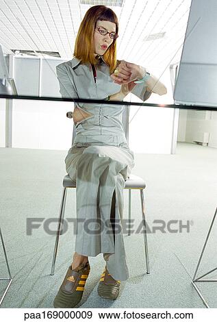 Woman sitting at desk, looking at watch View Large Photo Image Stock Photo - Woman sitting at desk, looking at watch. Fotosearch