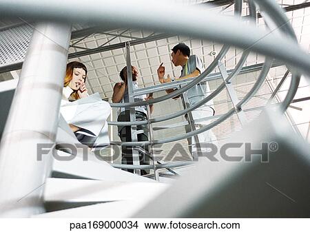 Woman sitting on stairs with cell phone, people standing above, low angle view View Large Photo Image Picture - Woman sitting on stairs with cell phone, people standing above, low angle view. Fotosearch