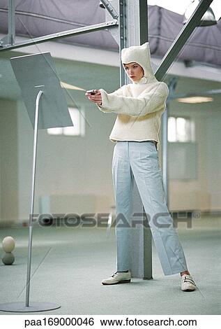 Stock Photograph - Woman wearing fleecy hooded sweater shooting beam from device in hands. Fotosearch