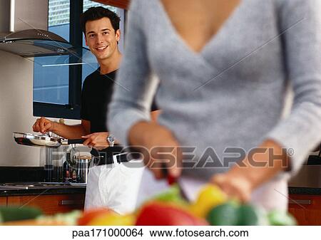 In kitchen, man holding pan, woman cutting vegetables in blurred foreground View Large Photo Image Picture - In kitchen, man holding pan, woman cutting vegetables in blurred foreground. Fotosearch