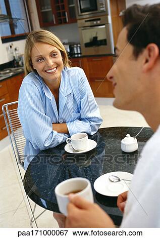 Stock Photo - Man and woman at table with cups and saucers, rear view of man, blurred, focus on woman smiling in background. Fotosearch