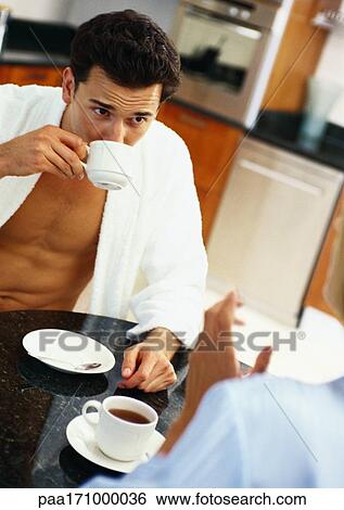 Man and woman sitting at table, man drinking from teacup, partial view of woman in foreground View Large Photo Image Stock Photograph - Man and woman sitting at table, man drinking from teacup, partial view of woman in foreground. Fotosearch