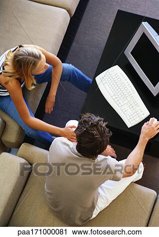 Stock Image - Man and woman sitting in living room using computer, high angle view. Fotosearch