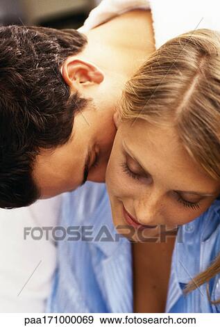 Stock Photo - Man leaning over woman's shoulder, kissing woman's neck, close-up. Fotosearch