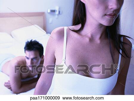 Stock Photo - Man lying on bed, woman in foreground, close-up. Fotosearch