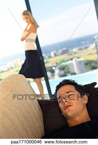 Man sleeping on sofa, woman in background View Large Photo Image Stock Photograph - Man sleeping on sofa, woman in background. Fotosearch