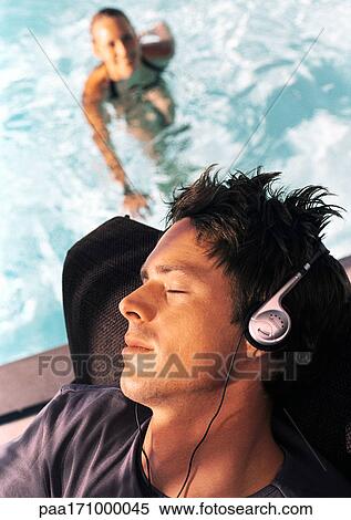 Man wearing headphones, woman in swimming pool in background, high angle view View Large Photo Image Stock Photography - Man wearing headphones, woman in swimming pool in background, high angle view. Fotosearch