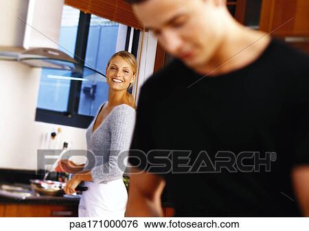 Woman in kitchen, smiling toward man in blurred foreground View Large Photo Image Stock Photograph - Woman in kitchen, smiling toward man in blurred foreground. Fotosearch