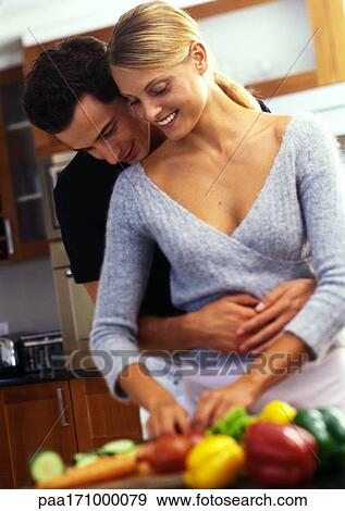 Woman standing at counter covered with vegetables, man behind woman with arms around her waist View Large Photo Image Stock Photo - Woman standing at counter covered with vegetables, man behind woman with arms around her waist. Fotosearch
