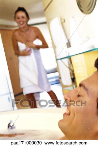 Stock Image - Woman wearing bath towel, man taking a bath. Fotosearch