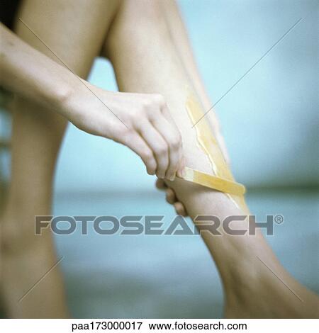 Stock Photo - Woman applying depilatory wax to leg, low section. Fotosearch