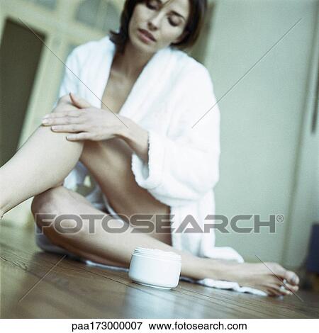 Stock Photo - Woman sitting on floor, moisturizing legs, low angle view. Fotosearch