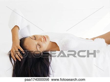 Stock Photograph - Woman lying on bed with eyes closed. Fotosearch