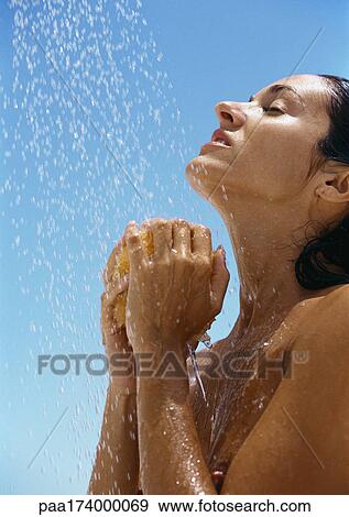 Stock Photo - Woman under shower, hands under head holding sponge, side view, close-up. Fotosearch