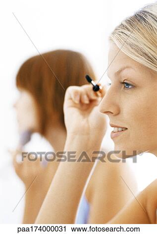 Stock Image - Women putting making up on, side view, blurred background. Fotosearch
